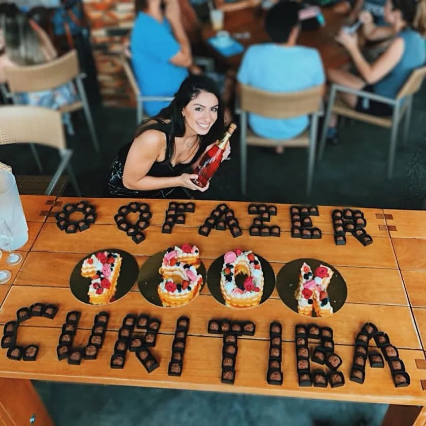 Comemoração dos 100 mil seguidores do O Que Fazer Curitiba: mesa de restaurante com bolos formando "100K" e bombons escrevendo "O Que Fazer Curitiba".