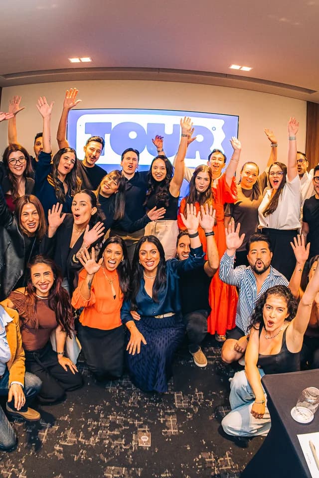 Time do Grupo Luz reunido de braços erguidos, comemorando em frente à tela com o novo logo do Tour.